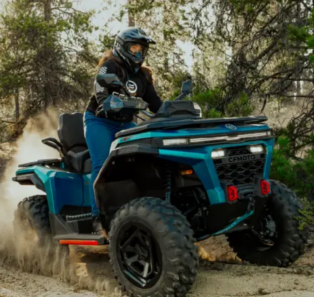 Femme conduisant un VTT CFMOTO CFORCE C6 PRO sur un sentier sablonneux en forêt, soulevant du sable.